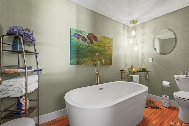 full bath with a freestanding tub, toilet, baseboards, and wood finished floors