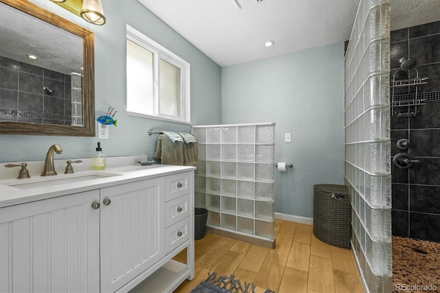 full bathroom with vanity, wood finished floors, baseboards, walk in shower, and a textured ceiling