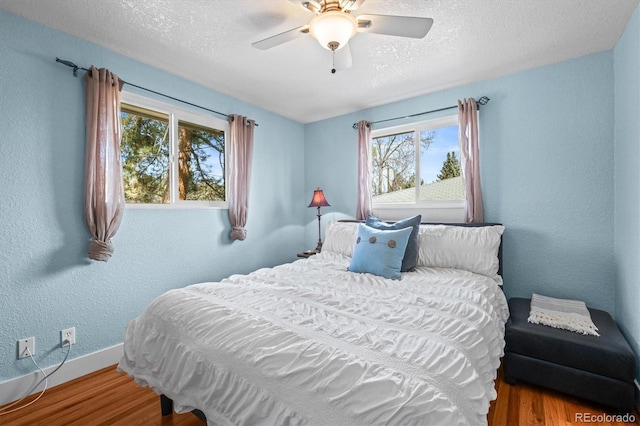 bedroom with a ceiling fan, wood finished floors, baseboards, a textured ceiling, and a textured wall