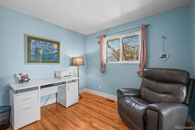 home office featuring visible vents, a textured ceiling, baseboards, and light wood-style floors