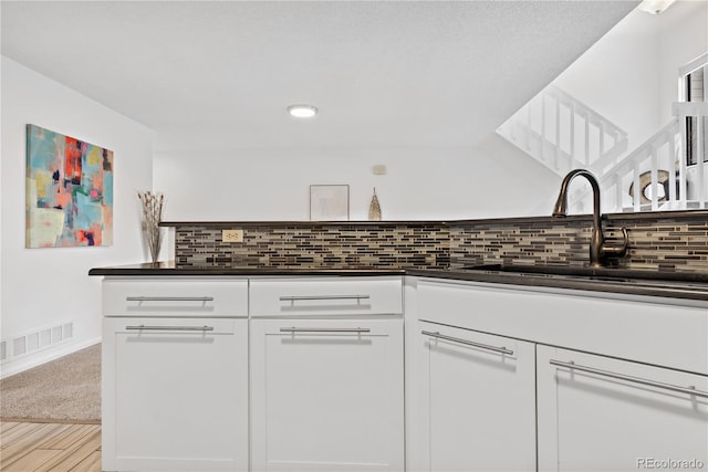 kitchen with tasteful backsplash, white cabinetry, sink, and light hardwood / wood-style floors