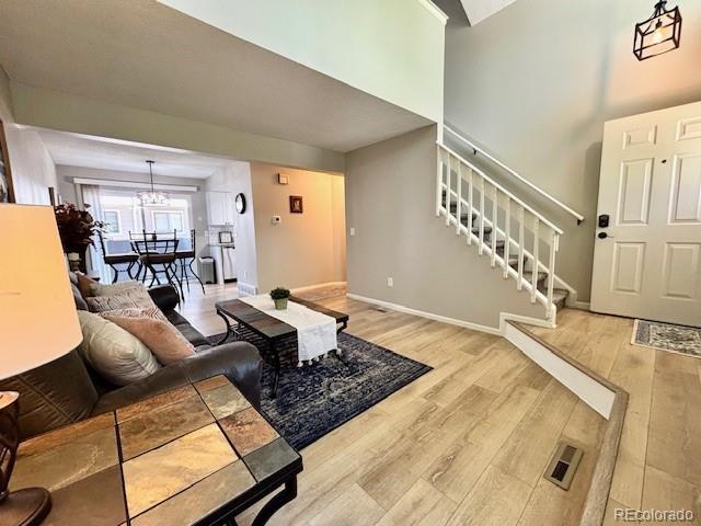6895 W 84th Way Unit 4, Arvada, CO 80003 - living room featuring wood finished floors, stairs, a chandelier, a high ceiling, and baseboards