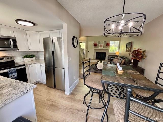 6895 W 84th Way Unit 4, Arvada, CO 80003 - kitchen featuring stainless steel appliances, white cabinetry, light wood finished floors, decorative backsplash, and a chandelier