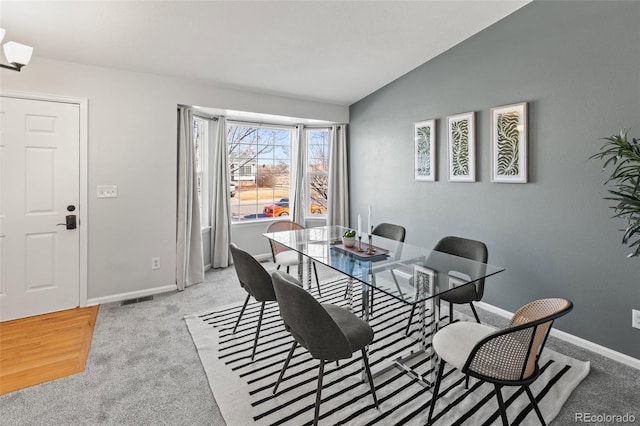 dining area featuring lofted ceiling, light carpet, visible vents, and baseboards