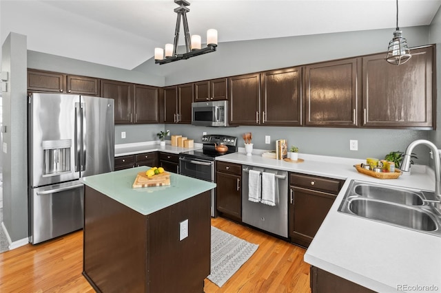 kitchen featuring stainless steel appliances, a sink, vaulted ceiling, dark brown cabinets, and light wood finished floors