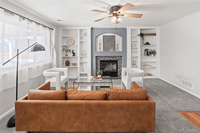 living area with built in shelves, baseboards, visible vents, and a tiled fireplace