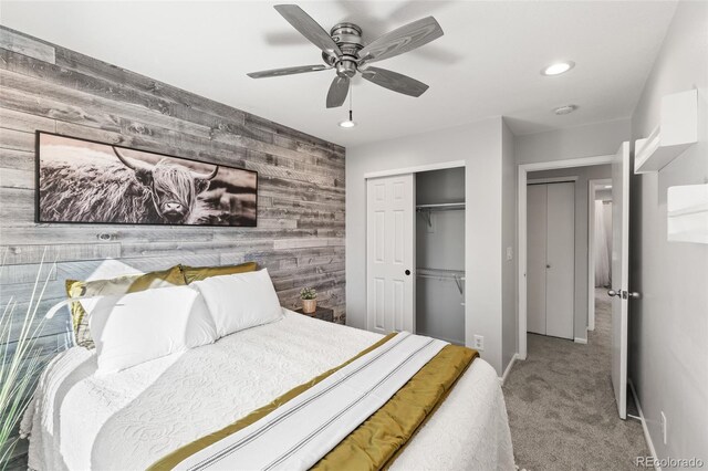 carpeted bedroom with wooden walls, baseboards, ceiling fan, an accent wall, and a closet