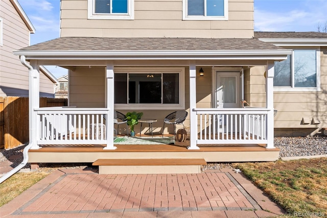 property entrance featuring fence, a porch, and roof with shingles