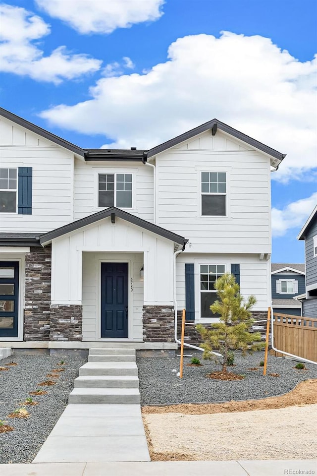 view of front of home featuring stone siding, board and batten siding, and fence