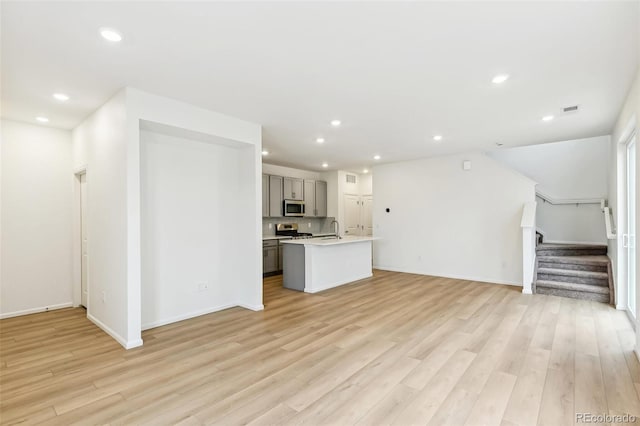 unfurnished living room featuring light wood-style floors, stairs, recessed lighting, and baseboards