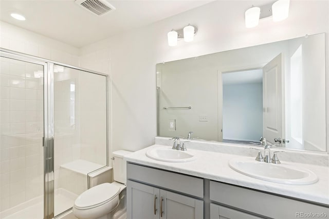 bathroom with a stall shower, toilet, and double vanity