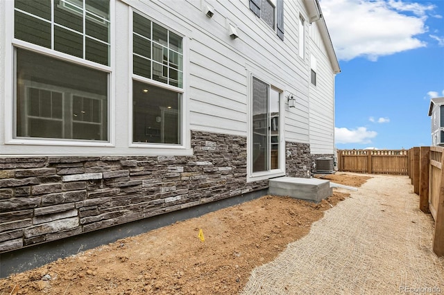 view of side of property with stone siding, a fenced backyard, and central air condition unit