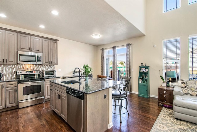 kitchen with a sink, dark stone counters, appliances with stainless steel finishes, a kitchen breakfast bar, and dark wood-style flooring