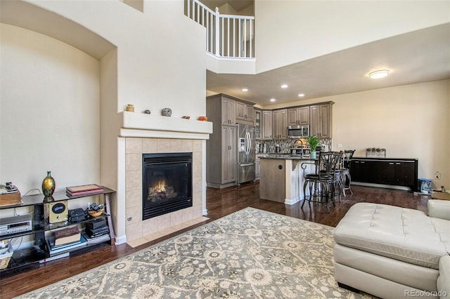 living room featuring a tiled fireplace, dark wood-type flooring, recessed lighting, and a towering ceiling