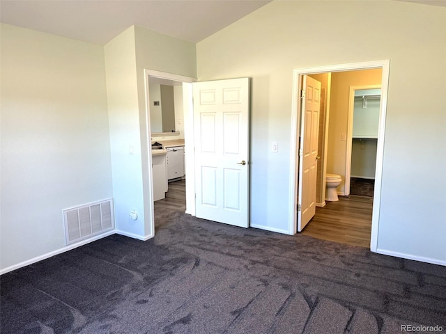 unfurnished bedroom featuring baseboards, vaulted ceiling, visible vents, and dark colored carpet