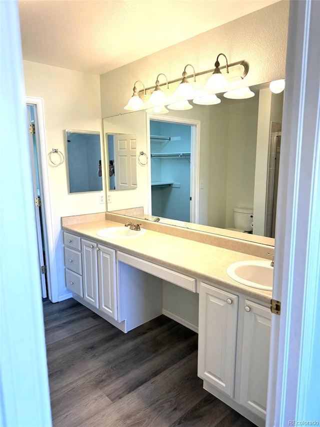 bathroom featuring toilet, double vanity, a sink, and wood finished floors