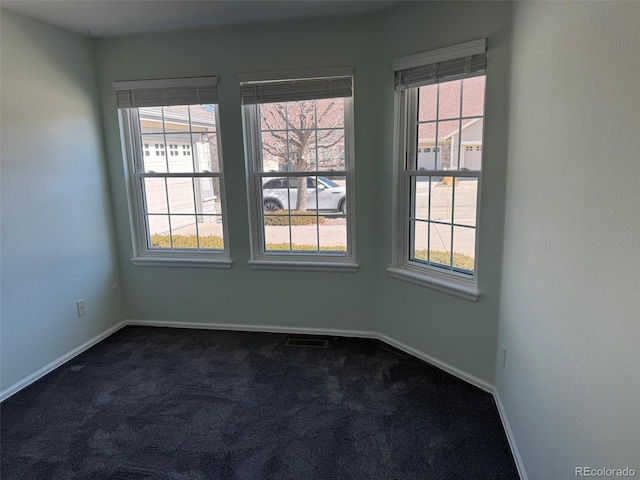 empty room with a wealth of natural light, dark carpet, and baseboards