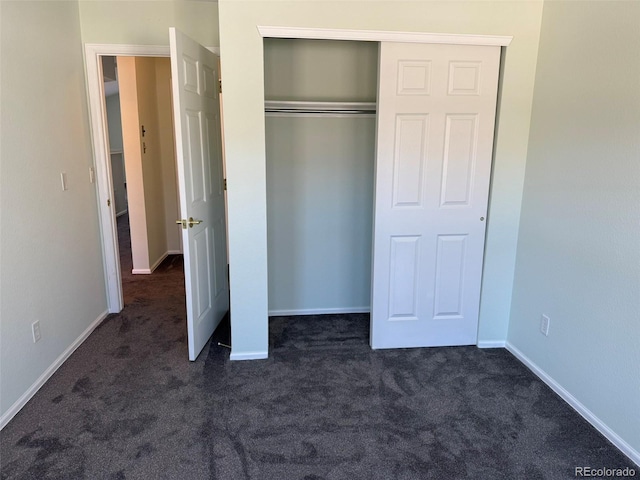 unfurnished bedroom featuring a closet, dark carpet, and baseboards