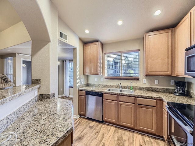 kitchen with sink, kitchen peninsula, stainless steel appliances, light stone countertops, and light hardwood / wood-style floors