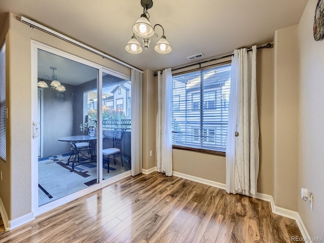 unfurnished dining area with plenty of natural light, wood-type flooring, and a notable chandelier