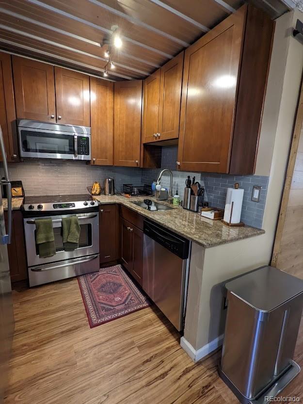 kitchen featuring decorative backsplash, appliances with stainless steel finishes, light stone countertops, light wood-type flooring, and a sink