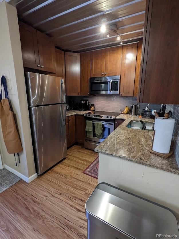 kitchen with backsplash, light stone countertops, appliances with stainless steel finishes, and light wood-type flooring