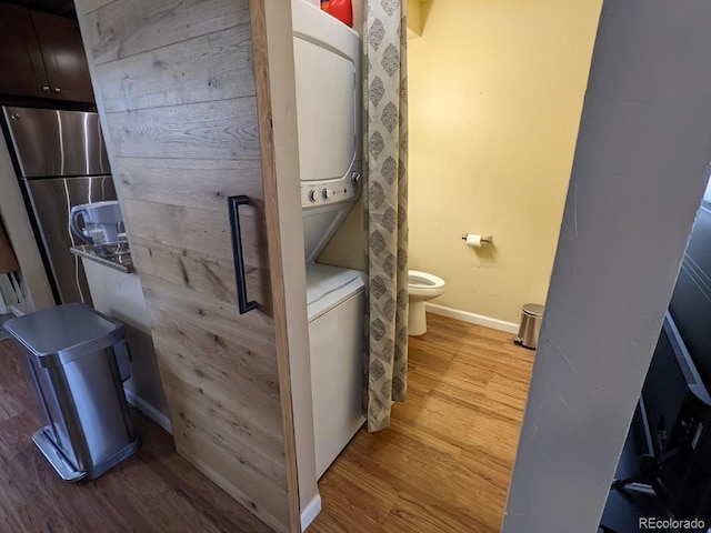 bathroom featuring baseboards, toilet, stacked washer / drying machine, and wood finished floors