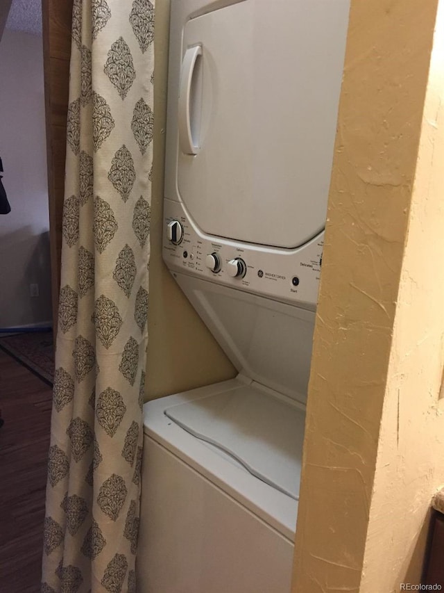 clothes washing area with stacked washing maching and dryer and wood finished floors