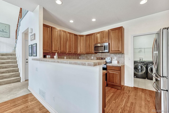 8943 Tappy Toorie Cir, Highlands Ranch, CO 80129 - kitchen with appliances with stainless steel finishes, independent washer and dryer, brown cabinetry, decorative backsplash, and light wood-style flooring