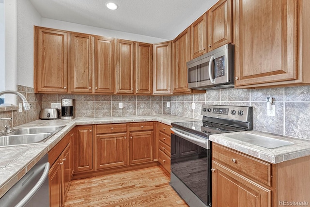 8943 Tappy Toorie Cir, Highlands Ranch, CO 80129 - kitchen with stainless steel appliances, a sink, light wood-style flooring, decorative backsplash, and brown cabinets