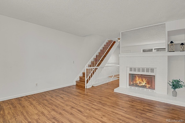 unfurnished living room featuring stairs, a brick fireplace, wood finished floors, baseboards, and a textured ceiling