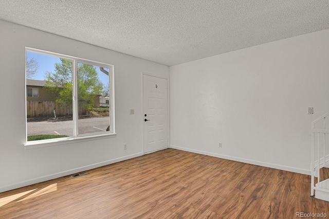 spare room featuring a textured ceiling, baseboards, wood finished floors, and visible vents