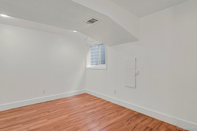 spare room with baseboards, vaulted ceiling, light wood-style flooring, and visible vents