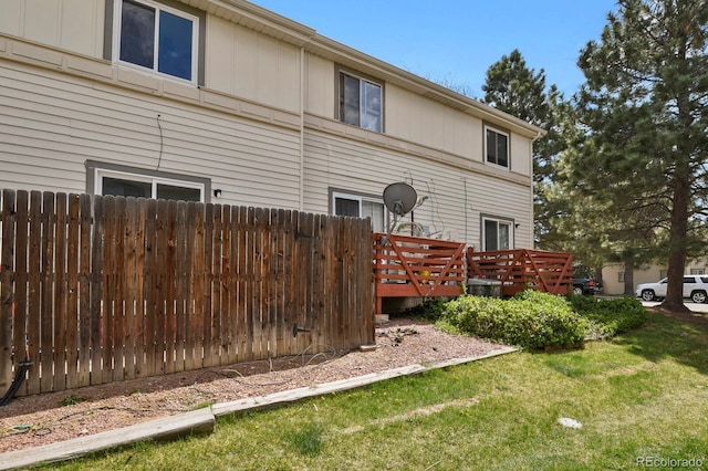 view of side of home with a lawn, a wooden deck, and fence