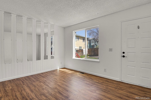 unfurnished room featuring a textured ceiling, visible vents, baseboards, and dark wood-type flooring