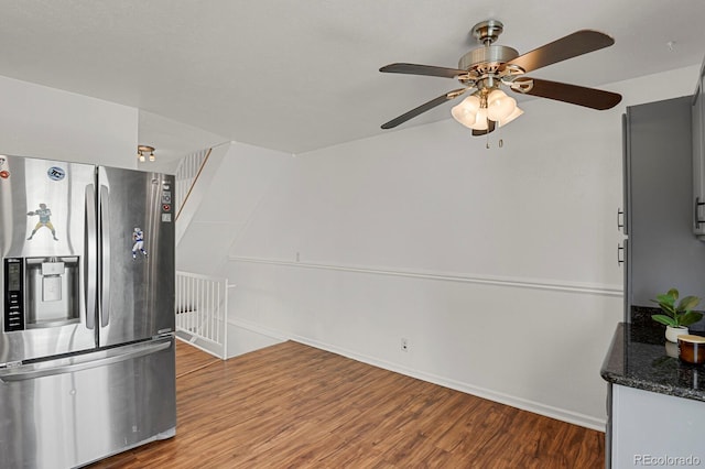 kitchen featuring wood finished floors, baseboards, stainless steel fridge, a ceiling fan, and dark stone countertops