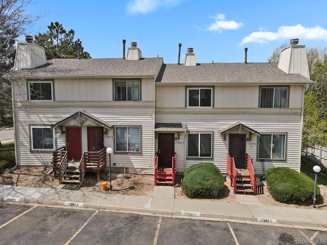 townhome / multi-family property featuring uncovered parking, roof with shingles, and a chimney