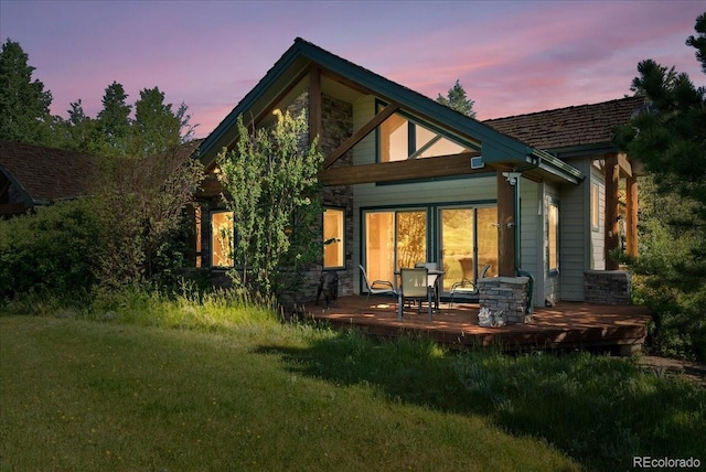 378 Fox Acres Dr W, Red Feather Lakes, CO 80545 - back of house at dusk featuring a lawn, stone siding, and a wooden deck