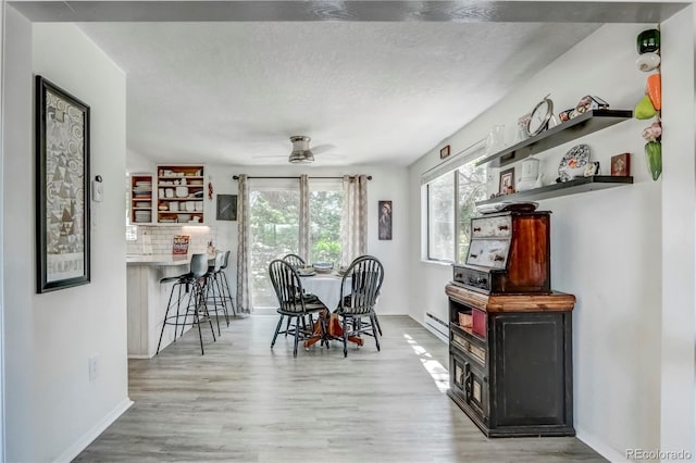 dining space featuring light hardwood / wood-style floors, a textured ceiling, baseboard heating, and ceiling fan