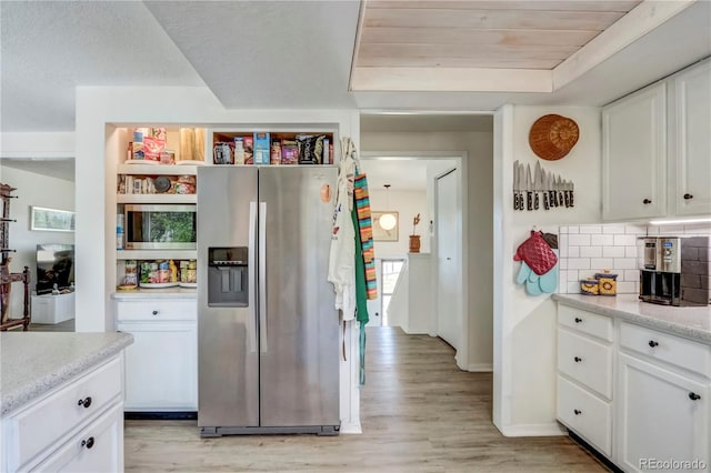 kitchen with light hardwood / wood-style flooring, a tray ceiling, white cabinets, stainless steel refrigerator with ice dispenser, and tasteful backsplash