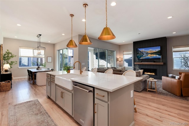 kitchen featuring decorative light fixtures, sink, a kitchen island with sink, light stone counters, and stainless steel dishwasher