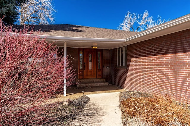 view of exterior entry with brick siding and roof with shingles