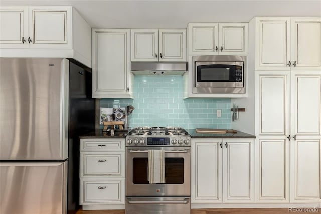 kitchen with dark countertops, backsplash, stainless steel appliances, and under cabinet range hood