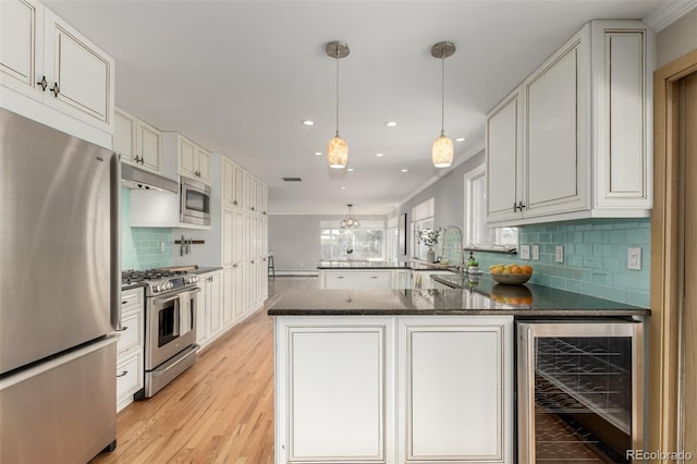 kitchen featuring light wood-style flooring, beverage cooler, backsplash, a peninsula, and appliances with stainless steel finishes