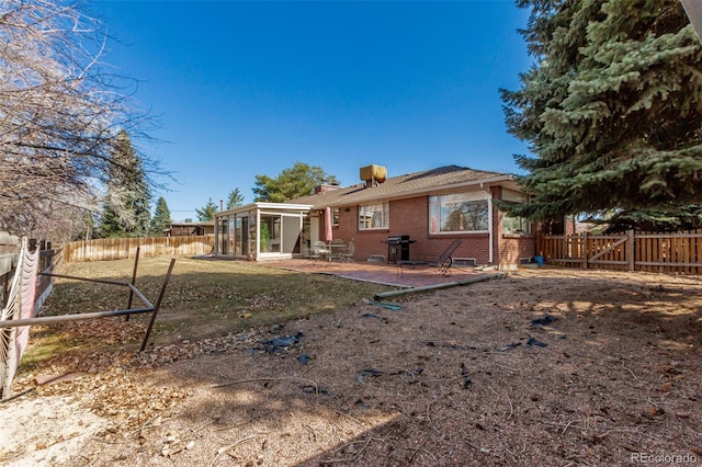 rear view of house featuring a patio, a fenced backyard, a sunroom, a chimney, and brick siding