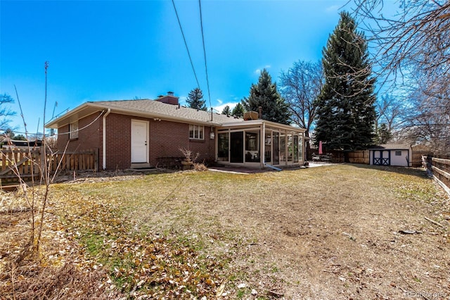 back of property featuring brick siding, a chimney, a storage shed, a sunroom, and an outbuilding