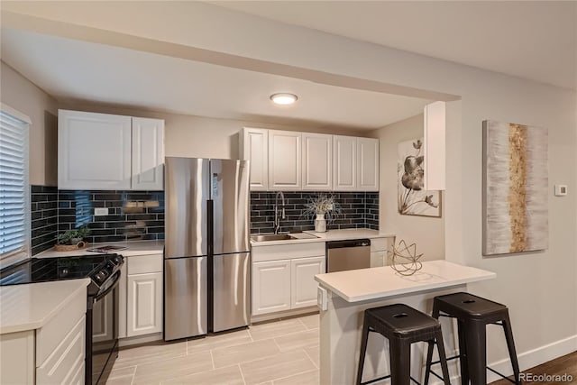 kitchen featuring decorative backsplash, a kitchen breakfast bar, stainless steel appliances, sink, and white cabinetry