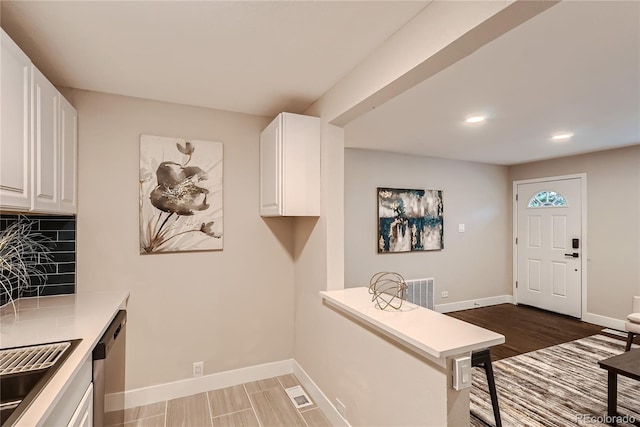 kitchen featuring white cabinets, stainless steel dishwasher, kitchen peninsula, and backsplash