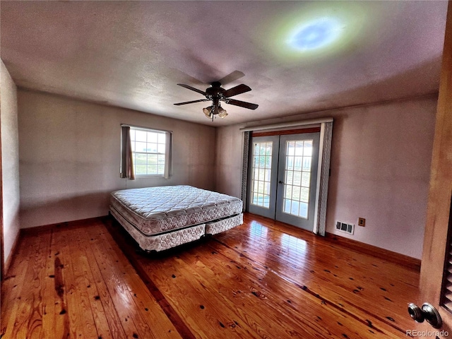 unfurnished bedroom featuring access to outside, multiple windows, hardwood / wood-style flooring, and ceiling fan