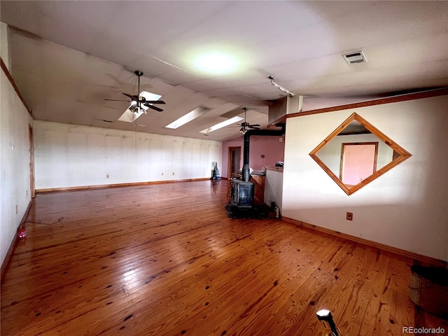 spare room featuring lofted ceiling with skylight, a wood stove, wood-type flooring, and ceiling fan